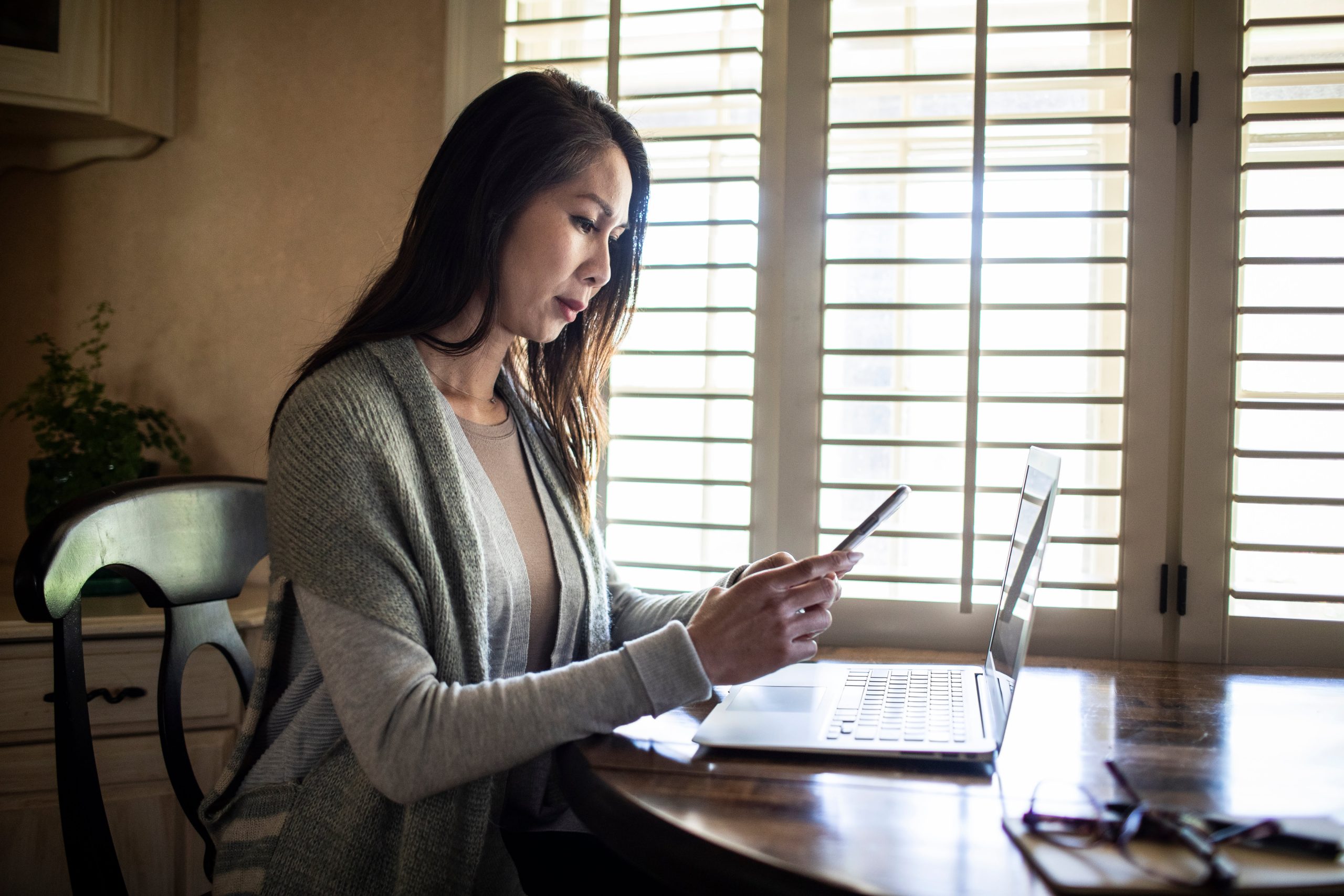 woman looking at phone and laptop
