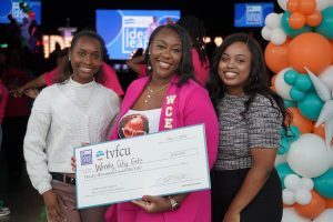 Three smiling women holding a large check.