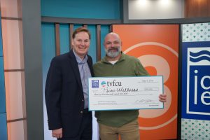 Two men in a TV studio holding a large check.