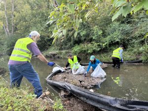 volunteers in water remove trash from litter boom