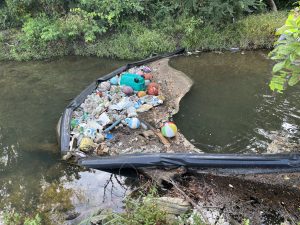 lots of trash caught in a litter boom in a creek